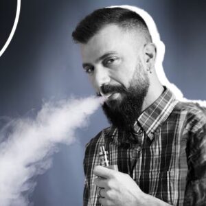 homem de barba e camisa xadrez soltando fumaça após fumar cigarro eletrônico.