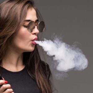 Mulher de cabelo comprido castanho e camiseta preta vaporando cigarro eletronico